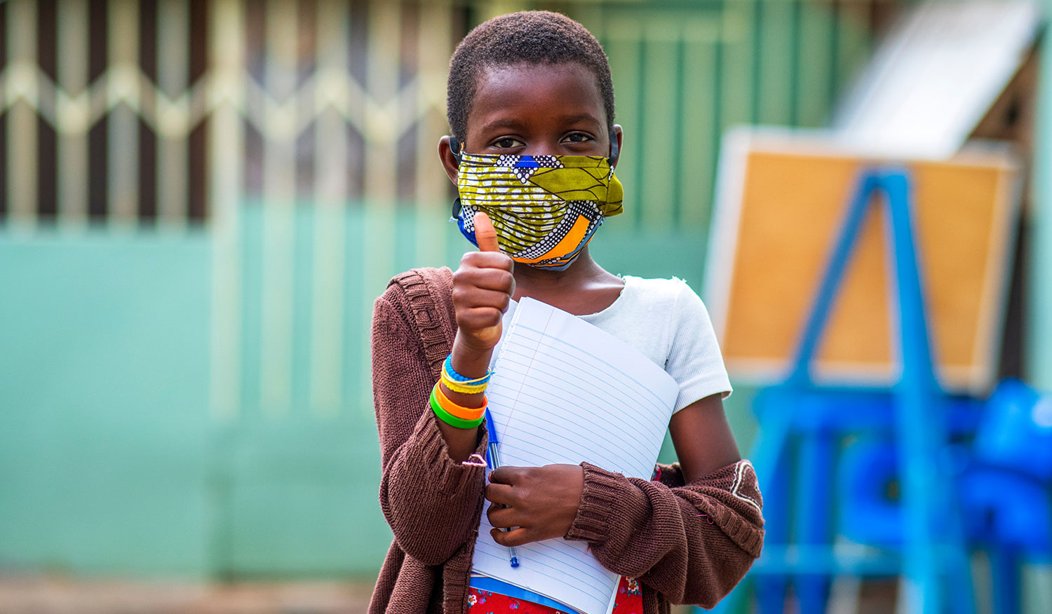 A young child wearing a colourful face mask gives a thumbs-up, representing international development