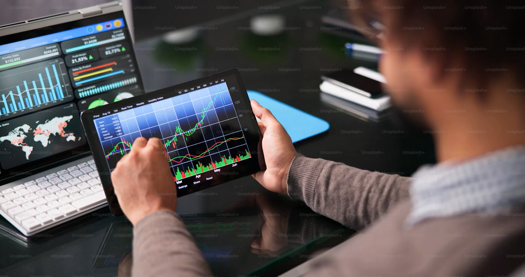 A person holds a tablet displaying data analytics charts, with additional dashboards visible on nearby screens