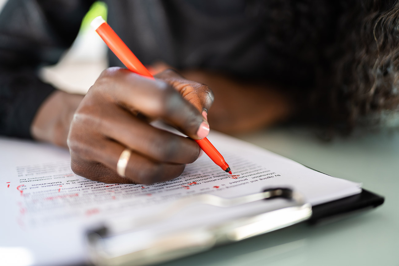 Close-up of an editor’s hand marking corrections on a printed manuscript with a red pen on a clipboard