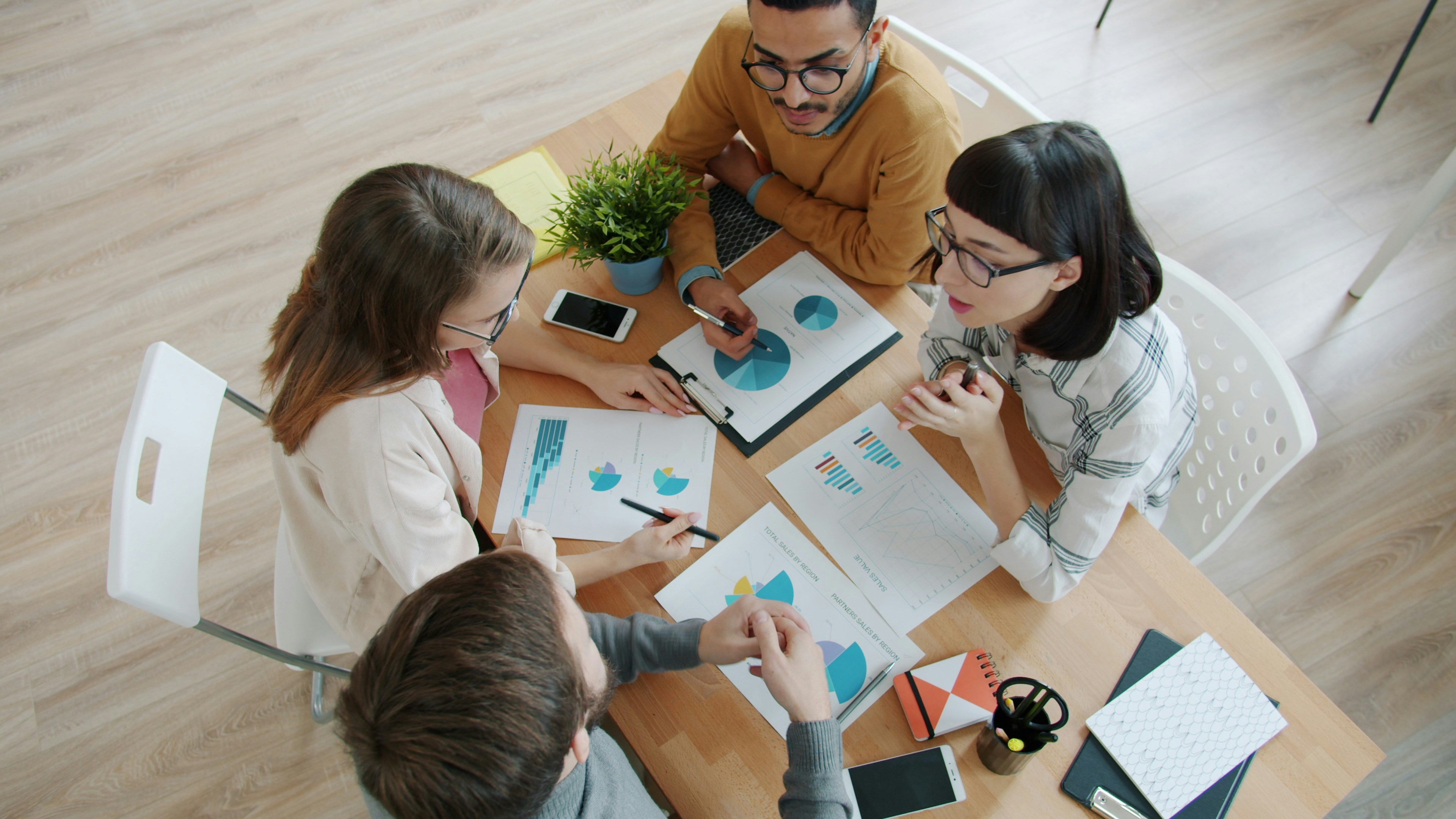Overhead view of four colleagues reviewing printed charts and graphs around a shared desk